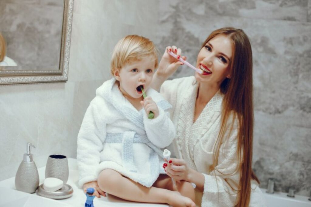 a kid is being taught how to brush by his mother- pediatric dentist in Dallas, TX